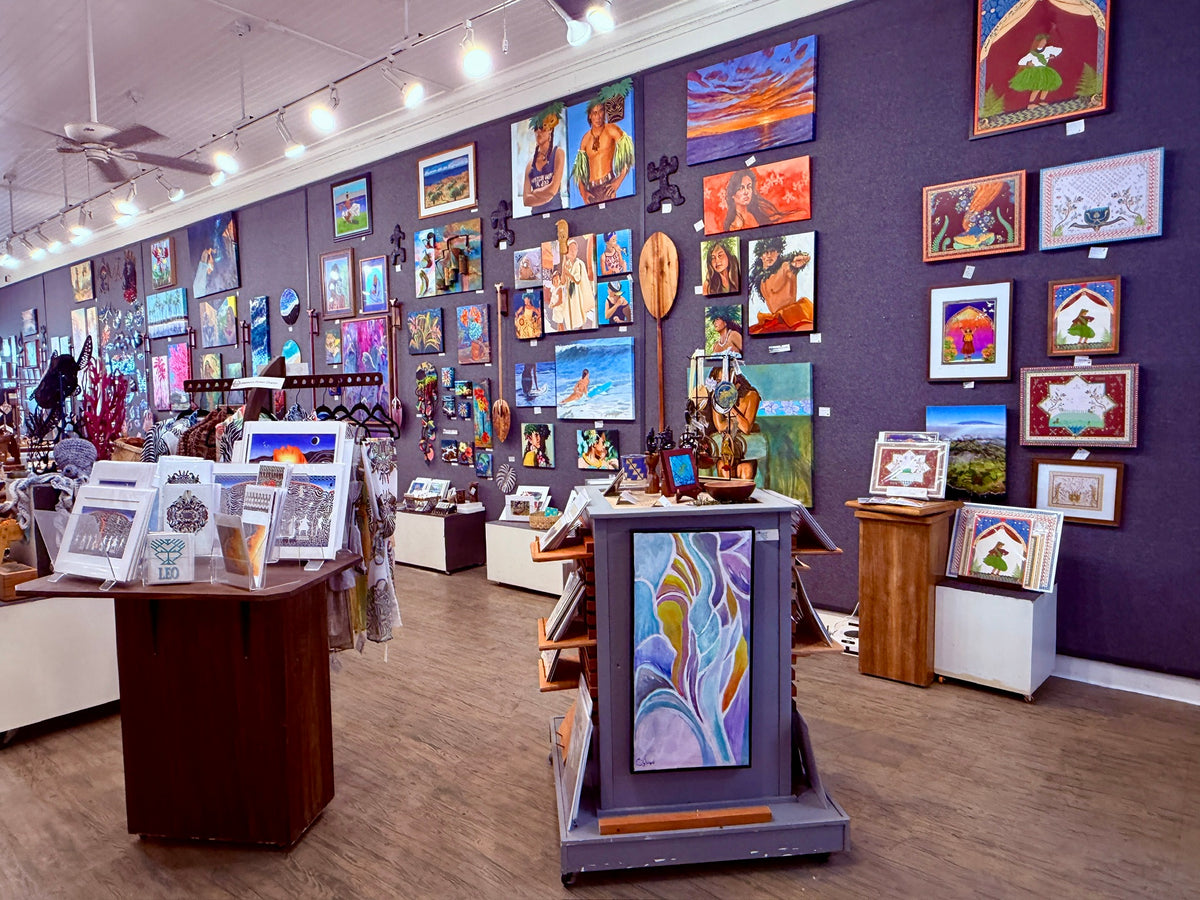 One Gallery interior with many colorful framed paintings and prints displayed on dark walls, along with display tables and wood flooring.